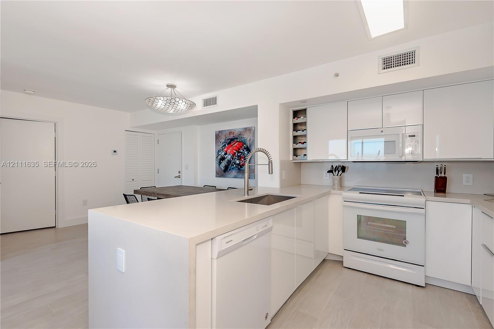 Kitchen featuring white high-gloss cabinetry, stone-surface countertops, a center island with an undermount sink, built-in wine storage, and light-toned wood-finish flooring