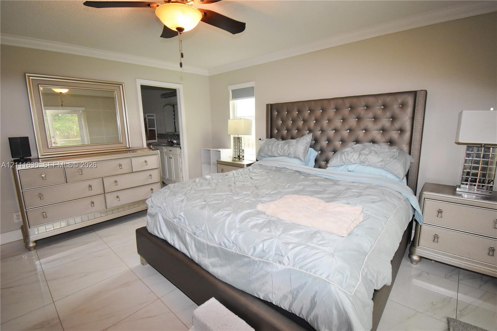 Neutral-toned room featuring large-format polished tile flooring, crown molding, and a central ceiling fan with an integrated light fixture