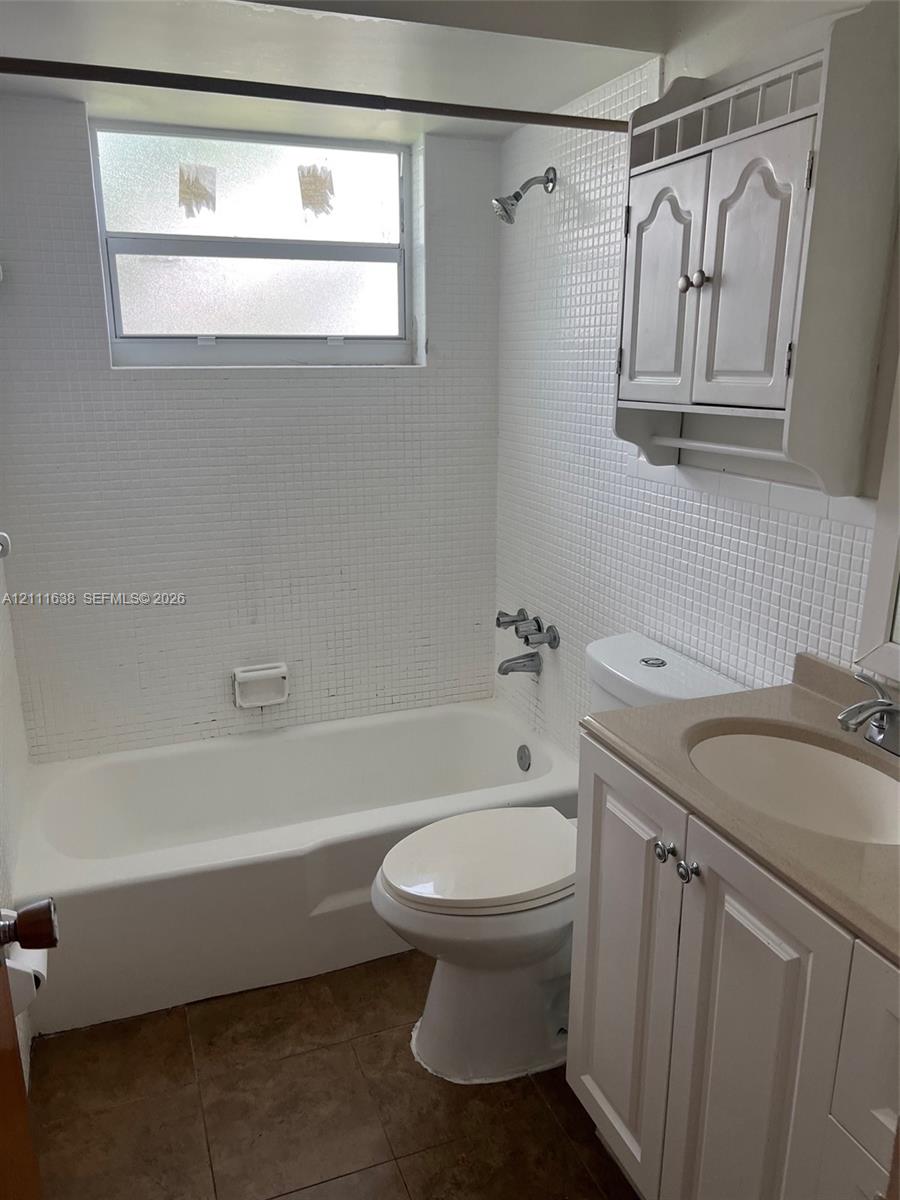Bathroom featuring a porcelain tub with white tiled surround, integrated white cabinetry, vanity with countertop basin, and wall-mounted storage unit