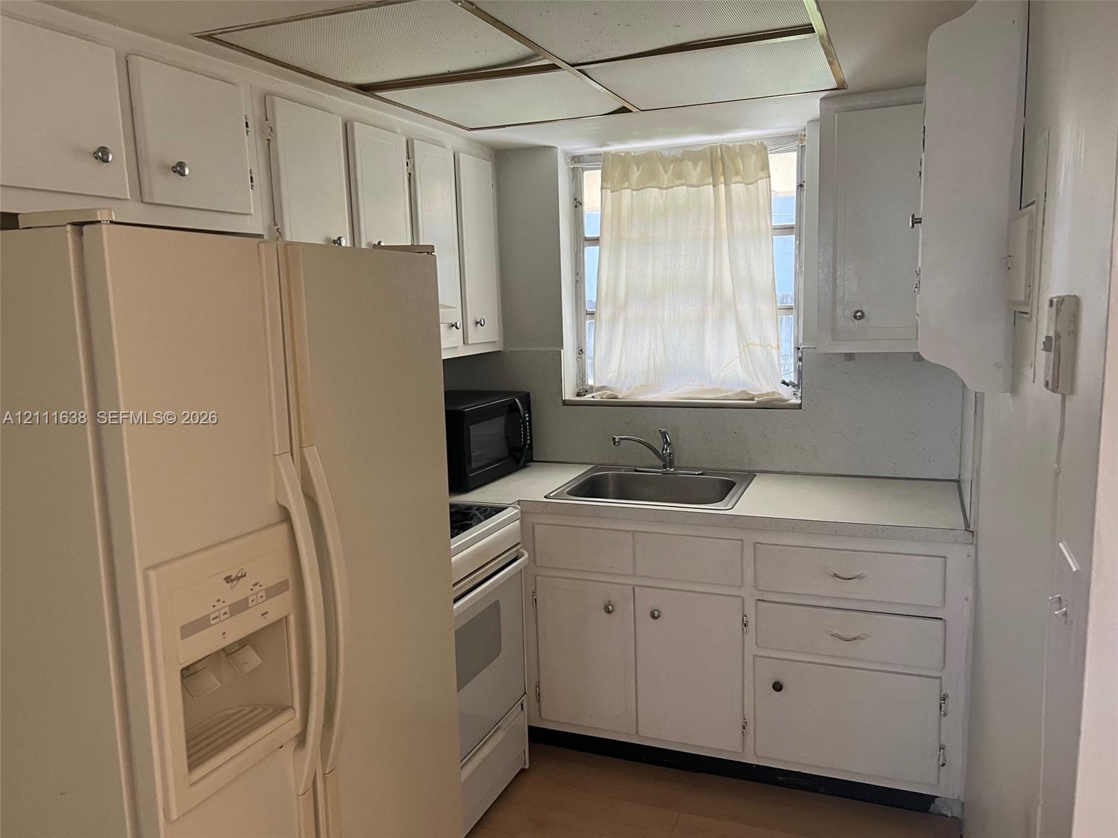 Kitchen featuring white cabinetry, solid-surface countertops, stainless steel sink with metal faucet, integrated range, and drop-ceiling panel lighting