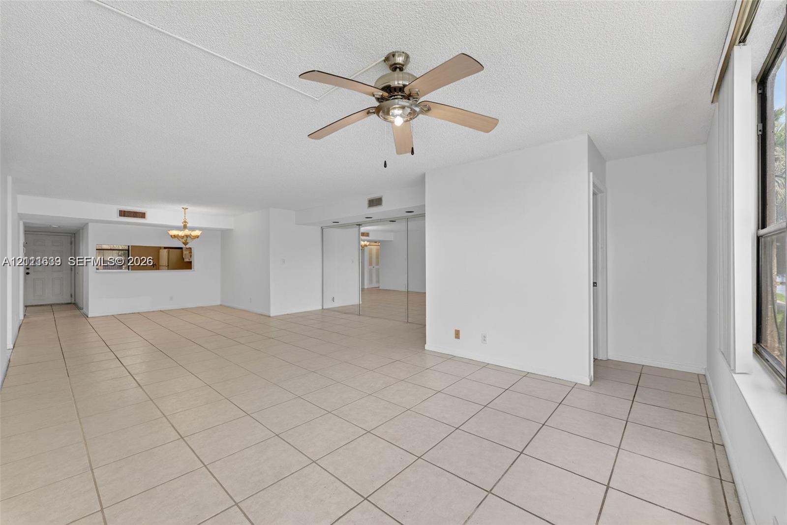 Spacious area featuring neutral-toned tile flooring, a ceiling fan with integrated lighting, mirrored closet doors, and an attached decorative chandelier