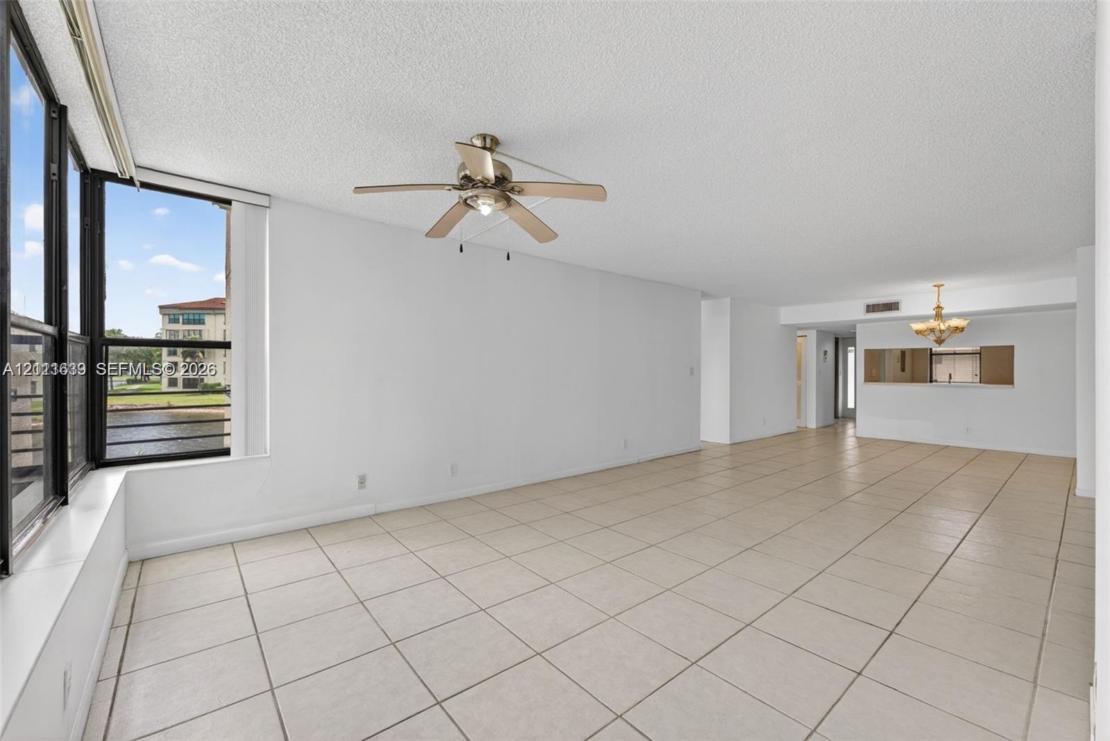 Open-concept interior featuring large-format tile flooring, oversized floor-to-ceiling windows, a ceiling fan with integrated lighting, and a decorative chandelier