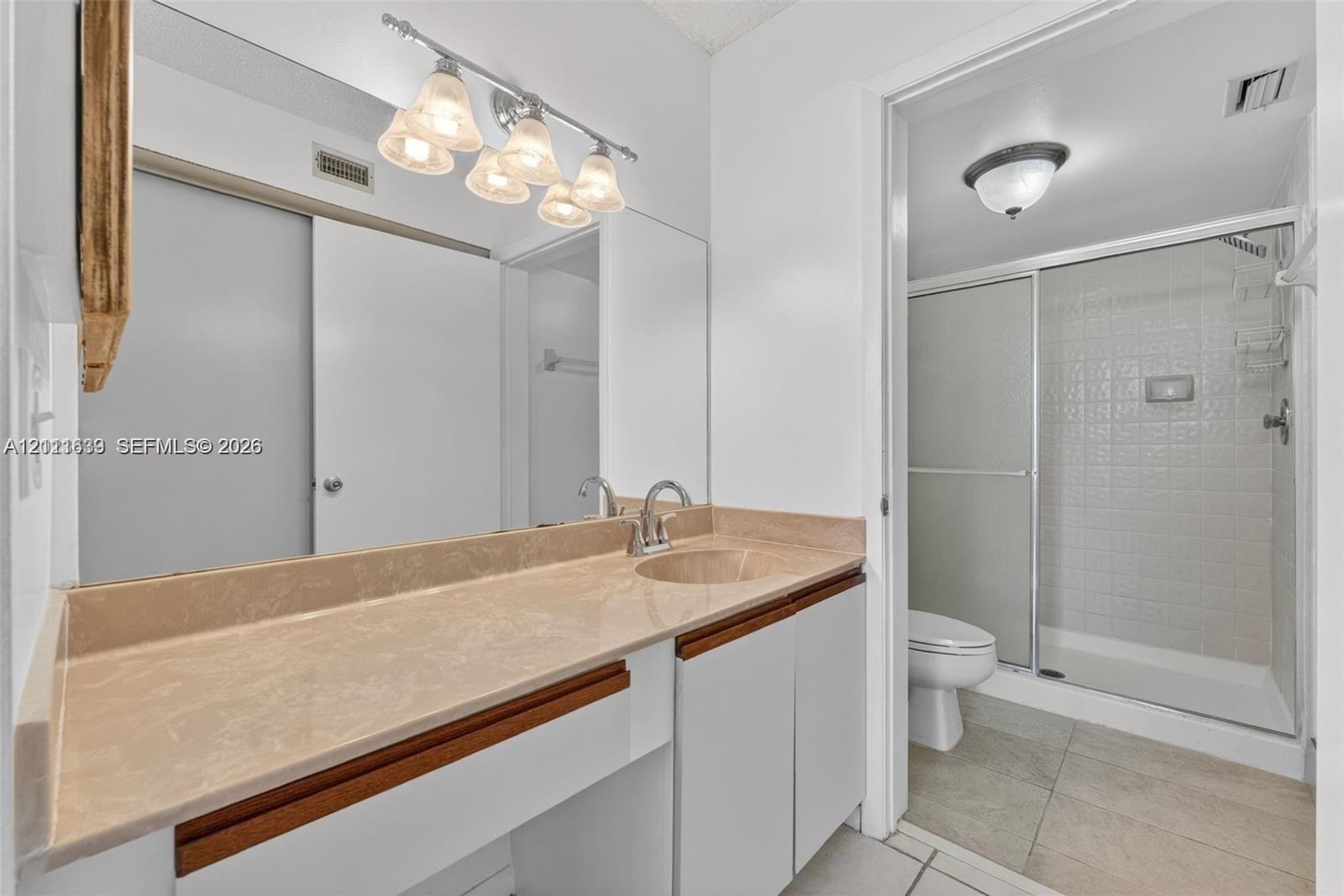 Bathroom featuring a wide vanity with a solid-surface countertop, an integrated sink, a full-width wall mirror, and a walk-in shower with a glass enclosure Bathroom featuring a wide vanity with a solid-surface countertop, an integrated sink, a full-width wall mirror, and a walk-in shower with a glass enclosure