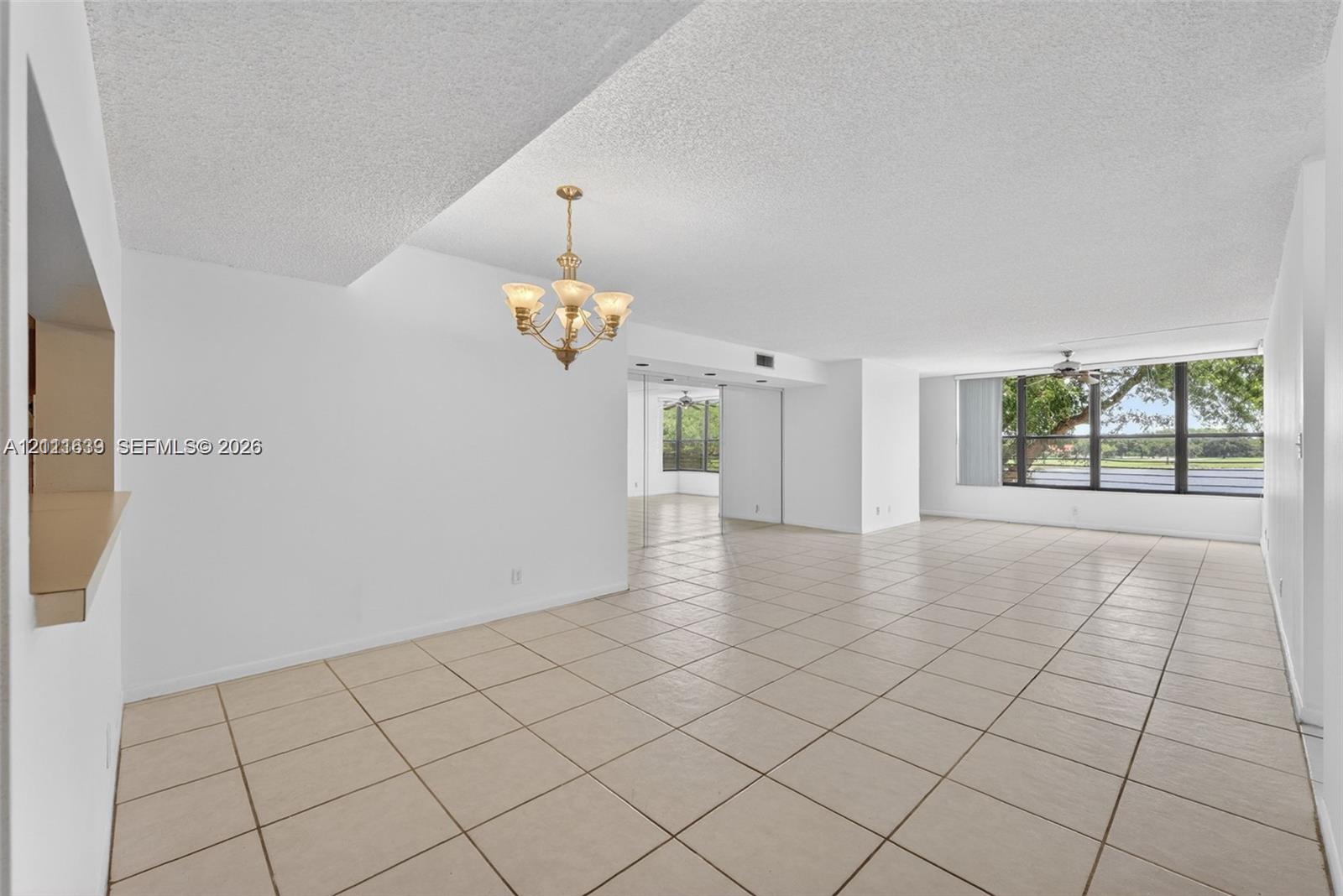 Open-concept space featuring ceramic tile flooring, multi-light decorative chandelier, expansive window wall, and built-in serving pass-through Open-concept space featuring ceramic tile flooring, multi-light decorative chandelier, expansive window wall, and built-in serving pass-through