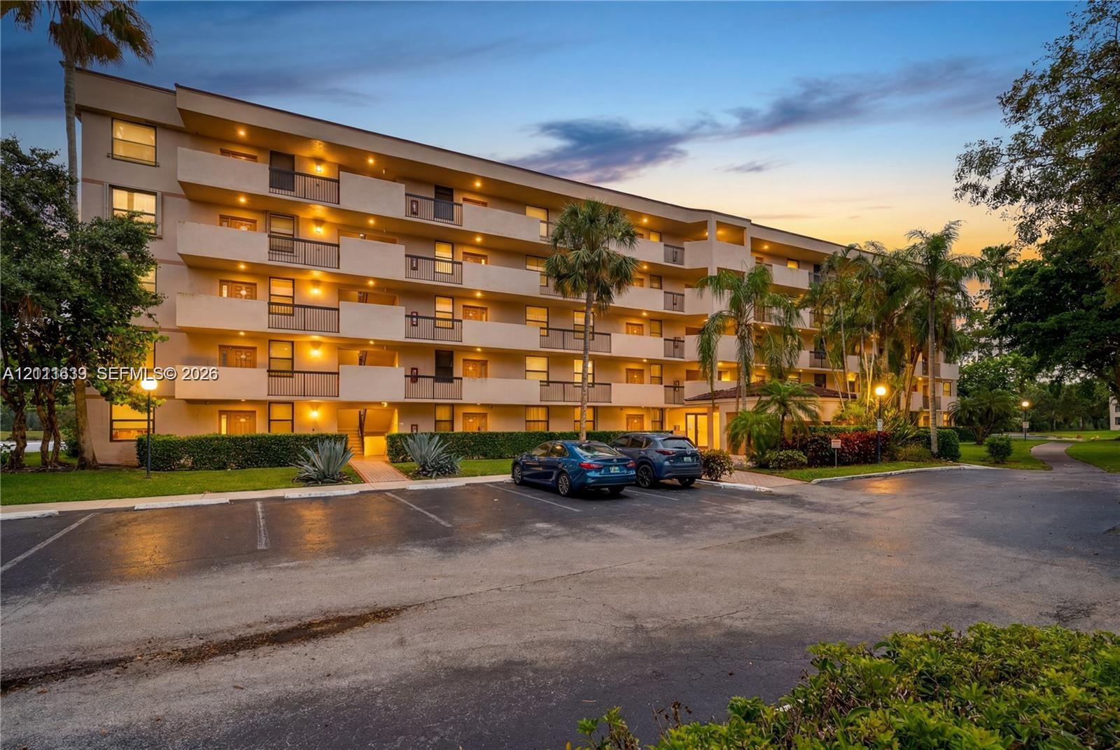 Multi-story residential building exterior featuring private balconies, asphalt parking area, and mature palm landscaping Multi-story residential building exterior featuring private balconies, asphalt parking area, and mature palm landscaping