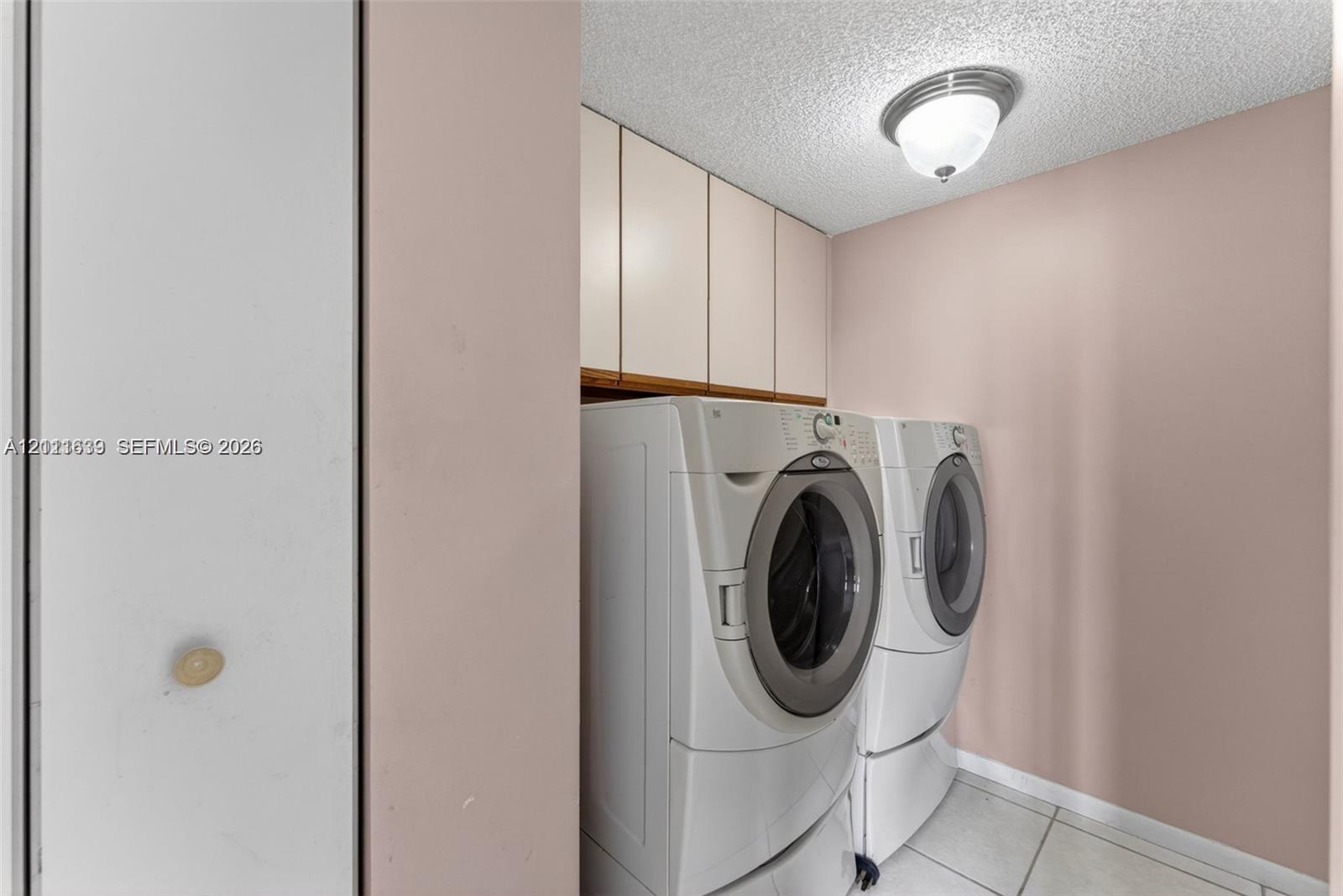 Laundry area featuring floor-to-ceiling built-in cabinetry, ceramic tile flooring, and a flush-mount ceiling light fixture Laundry area featuring floor-to-ceiling built-in cabinetry, ceramic tile flooring, and a flush-mount ceiling light fixture