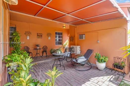 Covered patio featuring brick pavers, a metal frame overhead structure, and wall-mounted exterior lighting