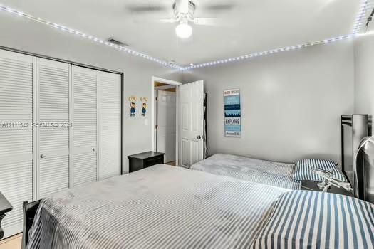 Bedroom featuring white louvered closet doors, a central ceiling fan with integrated lighting, and crown-molding recessed accent lighting
