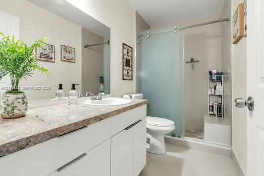 White cabinetry with flat-panel doors, stone-patterned countertop, integrated basin sink, and walk-in shower featuring a frosted glass sliding door