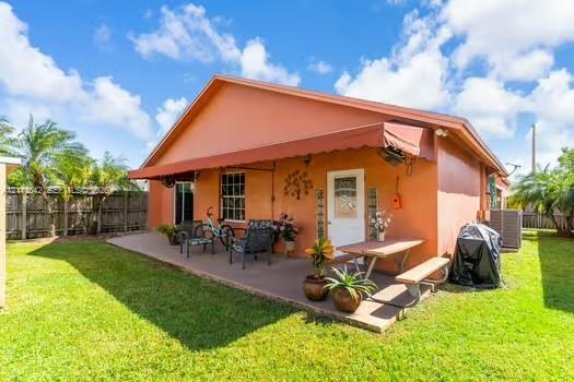Rear exterior featuring a concrete patio, retractable fabric awning, fenced perimeter, and established landscaping