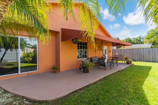 Covered concrete patio with a retractable awning, stucco exterior, sliding glass doors, and a fenced-in backyard