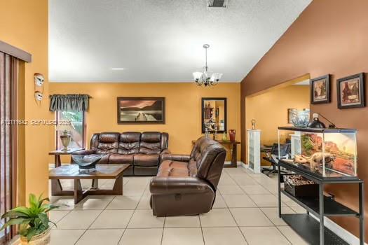 Living area featuring vaulted ceilings, light-toned ceramic tile flooring, a multi-arm chandelier, and a wide interior wall cutout