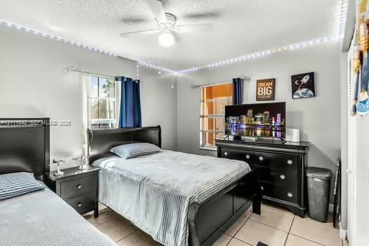Neutral-toned room featuring neutral ceramic tile flooring, dual windows with curtain rods, and a ceiling-mounted light fixture with a central fan