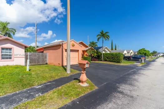 Single-story stucco exterior featuring a built-in garage, asphalt driveway, and ornamental pedestal mailbox