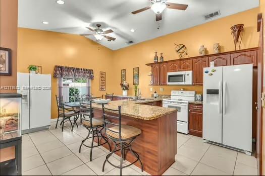 Kitchen featuring cathedral ceilings, custom wood cabinetry, an expansive island with a stone-composite countertop, tile flooring, and dual ceiling fans
