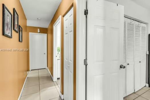 Interior hallway featuring neutral-toned ceramic tile flooring, solid-core interior doors, and white louvered-style closet doors