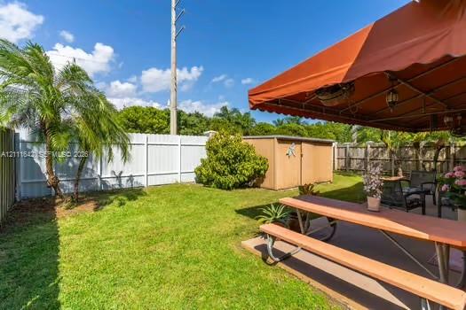 Fenced backyard featuring a manicured lawn, palm tree, concrete patio, and detached storage shed
