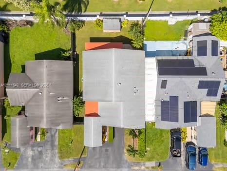 Aerial perspective featuring a multi-structure property with solar panel arrays, shingle roofing, paved driveways, and landscaped lawn areas