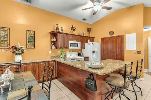 Kitchen featuring stone countertops, wood-finish cabinetry, an extended breakfast bar, tile flooring, and a vaulted ceiling with a mounted light-and-fan fixture