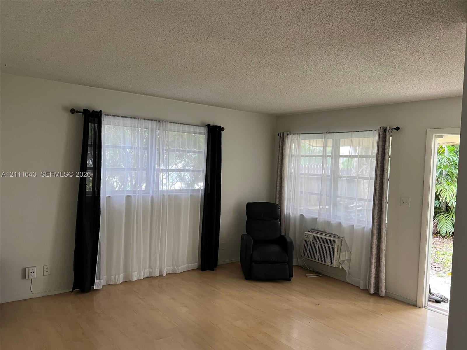 Interior area featuring wood-finish flooring, dual windows with grid detailing, and an integrated through-wall air conditioning unit