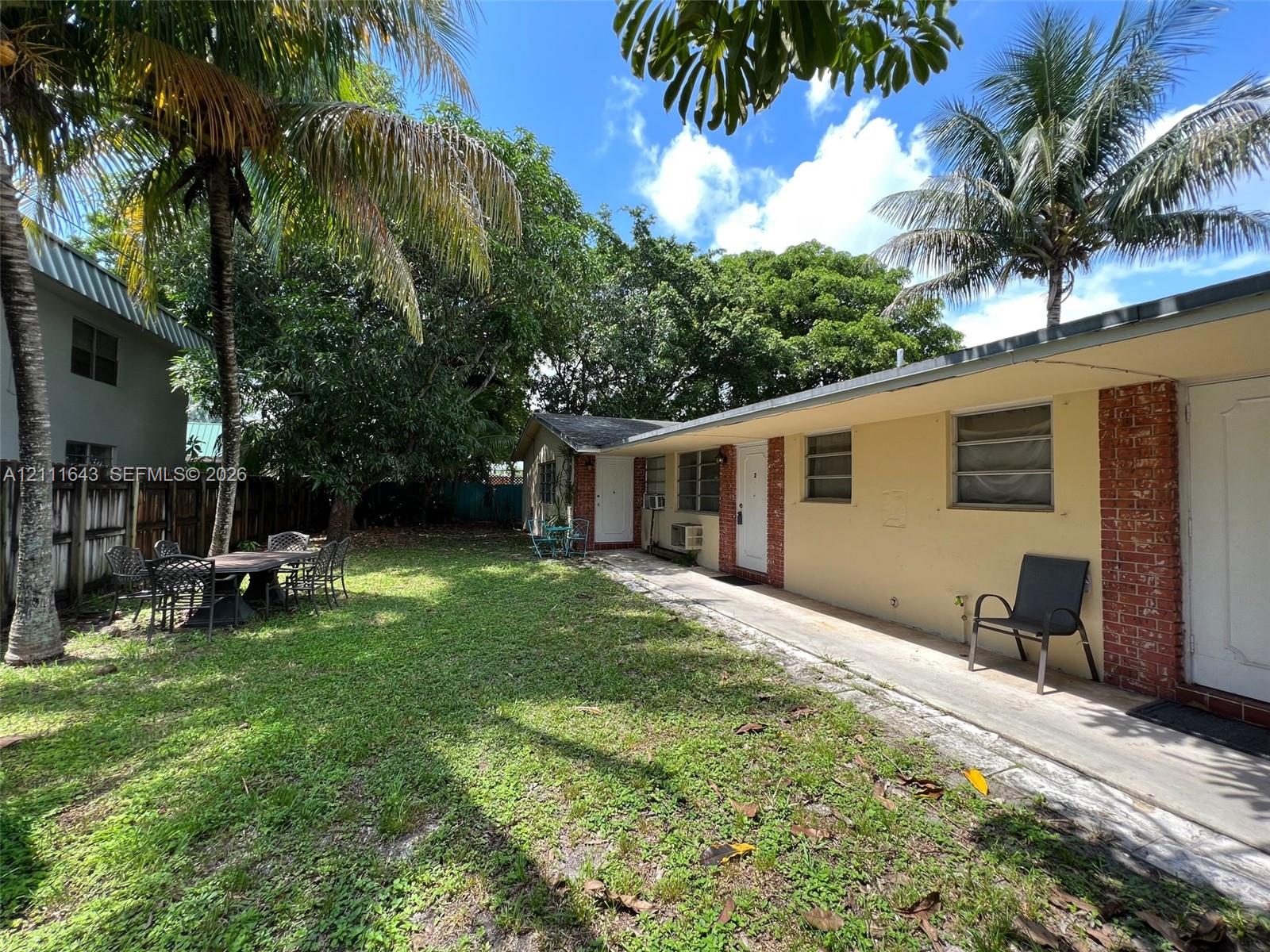 Rear exterior featuring a concrete walkway, brick masonry accents, mature palm trees, and a lawn area