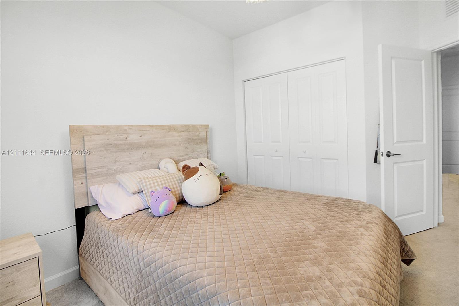 Neutral-toned room featuring light-colored wall-to-wall carpeting, high-reaching ceilings, and a built-in double-door closet with paneled detailing