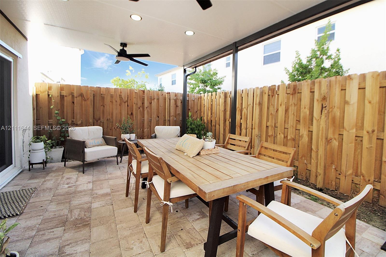 Covered patio featuring paver flooring, a wooden perimeter privacy fence, and a mounted ceiling fan with integrated lighting