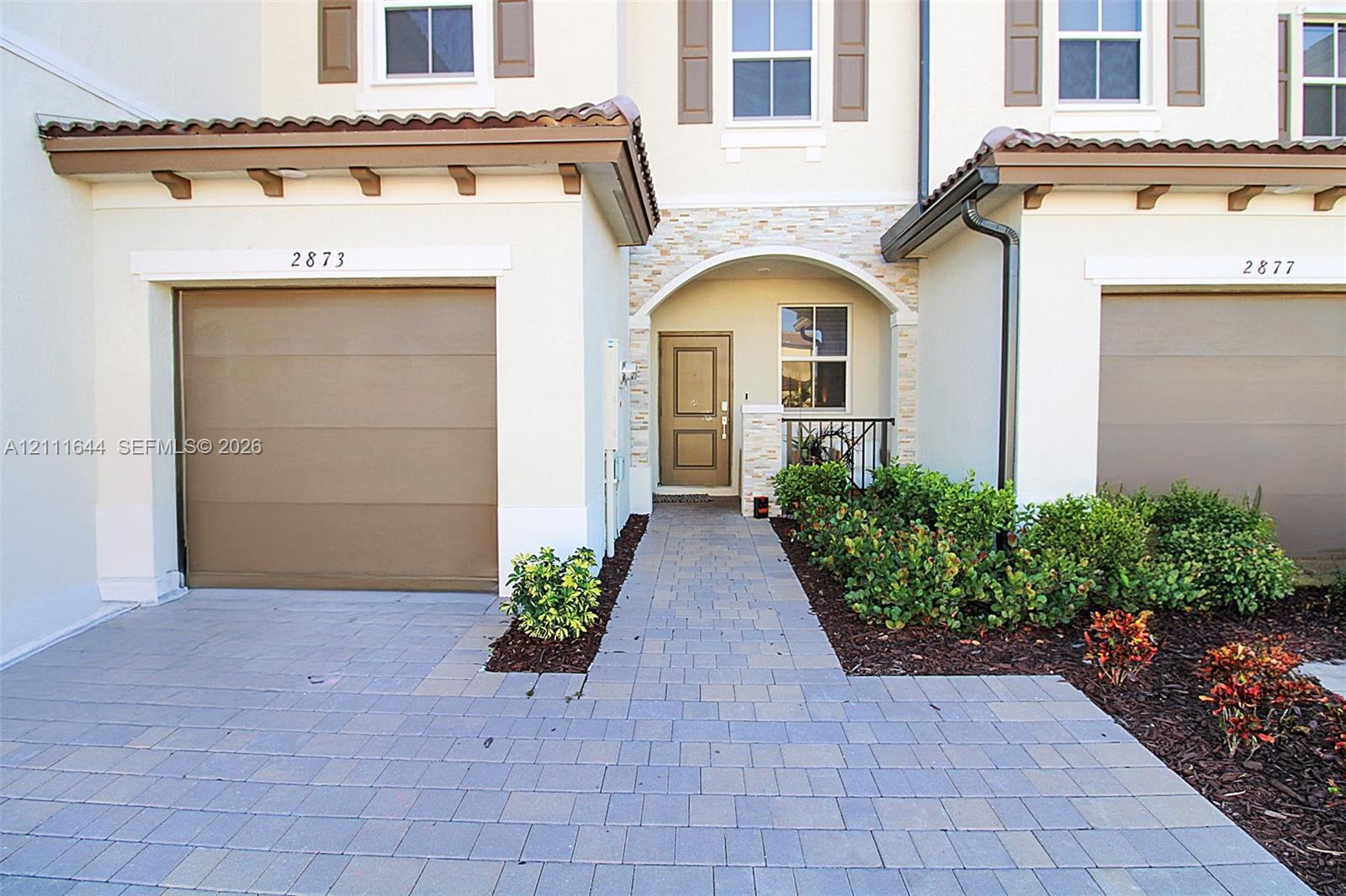 Exterior featuring a paver driveway, single-car garage, stone veneer entryway accents, and a covered portico with arched detailing
