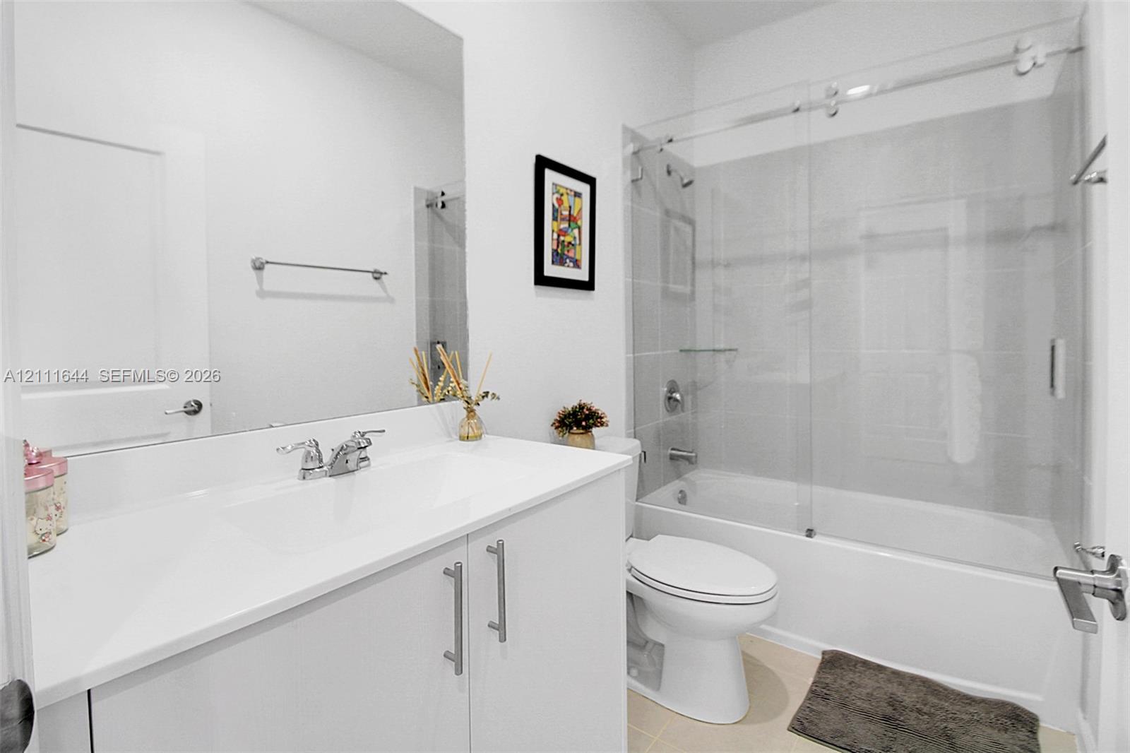 Bathroom featuring a white vanity with a composite countertop, an expansive frameless mirror, and a tub-shower combination enclosed by a sliding glass door with polished chrome hardware