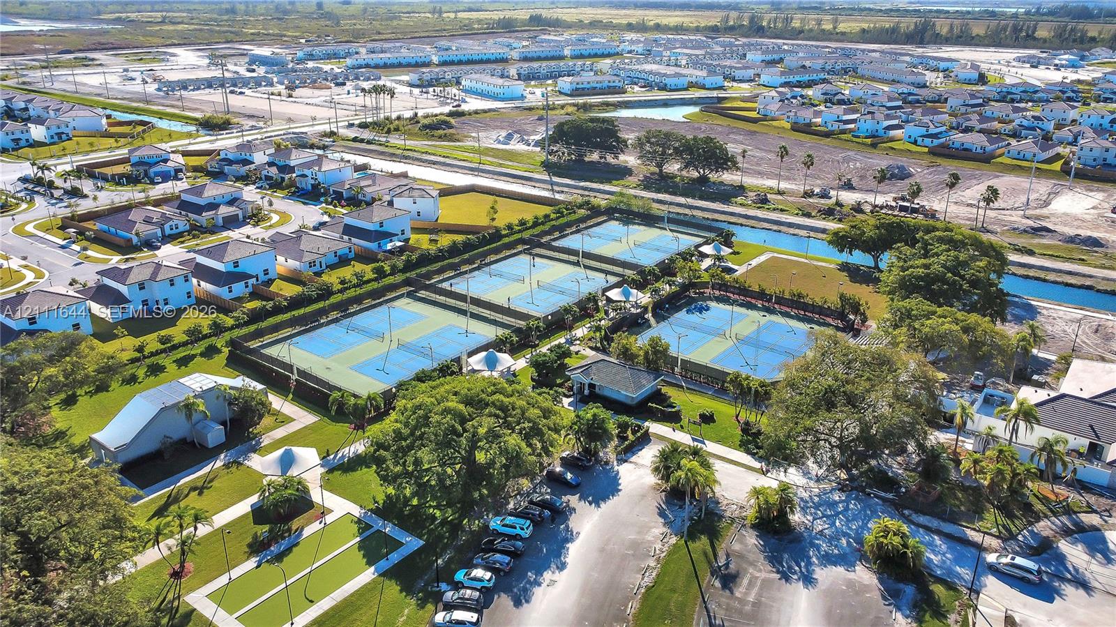 Aerial perspective of community recreational facilities featuring multiple tennis courts, pickleball courts, paved walking paths, and landscaped green spaces