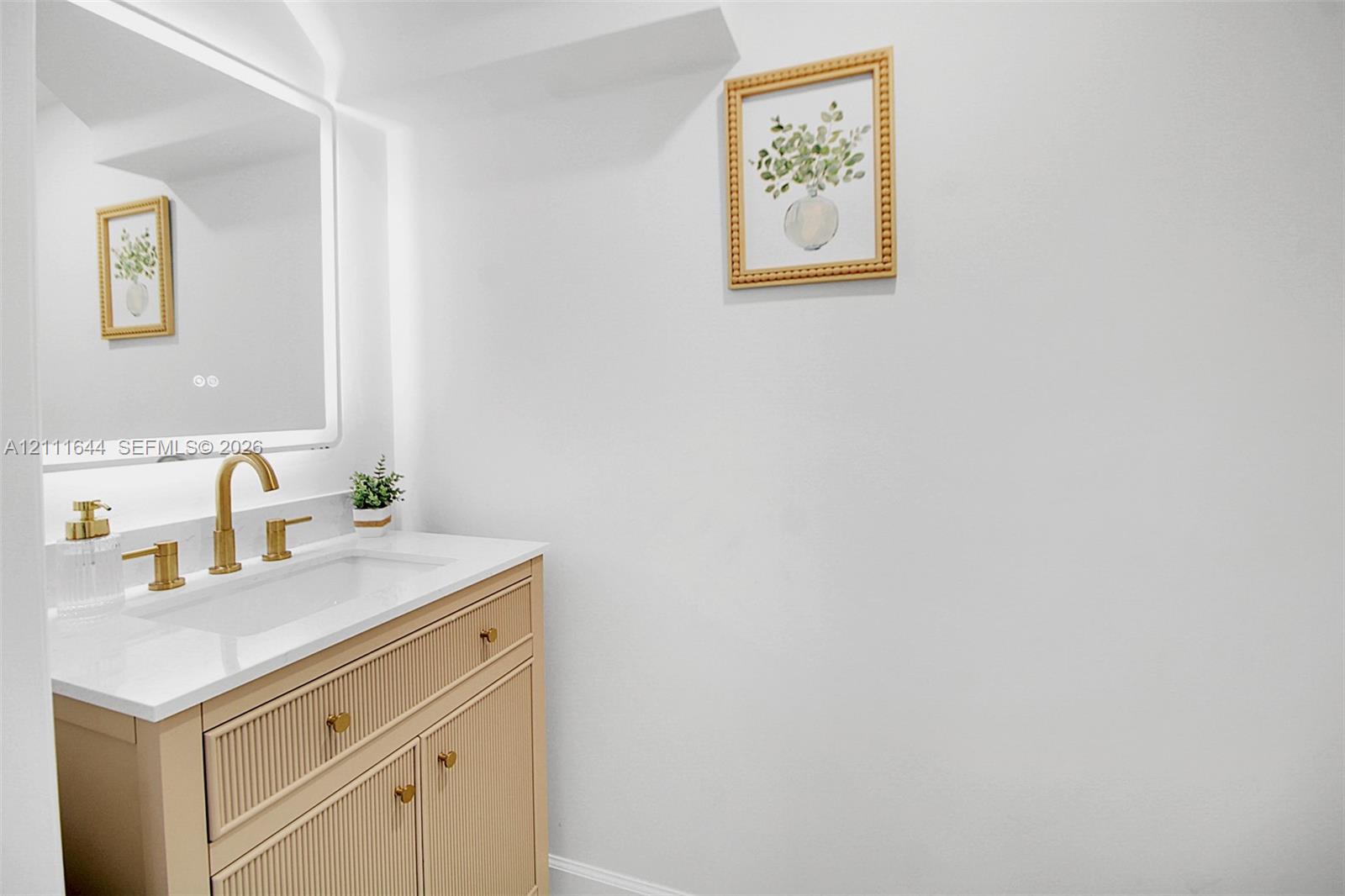 Fluted wood-finish vanity with a stone countertop, integrated rectangular sink, brass-toned faucet, and an LED-backlit mirror