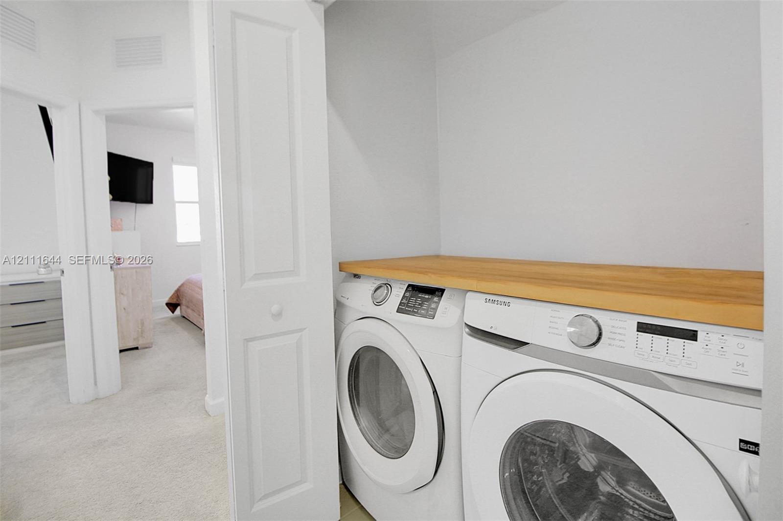 Laundry closet featuring stacked front-loading appliances and a built-in wood-finish folding counter