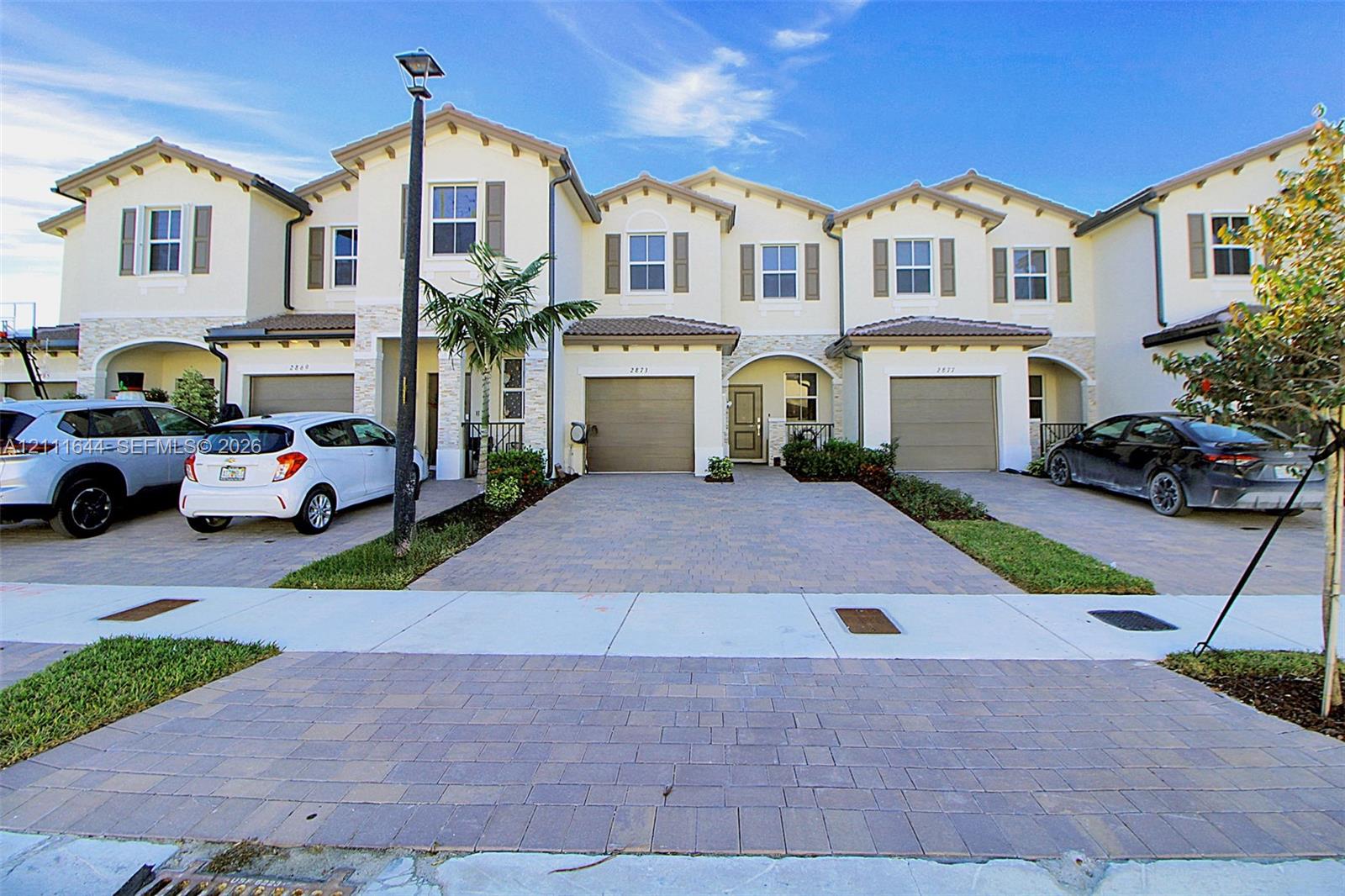 Multi-story townhome exterior featuring stucco facade, stone veneer accents, multi-gabled roofline, and paver driveways