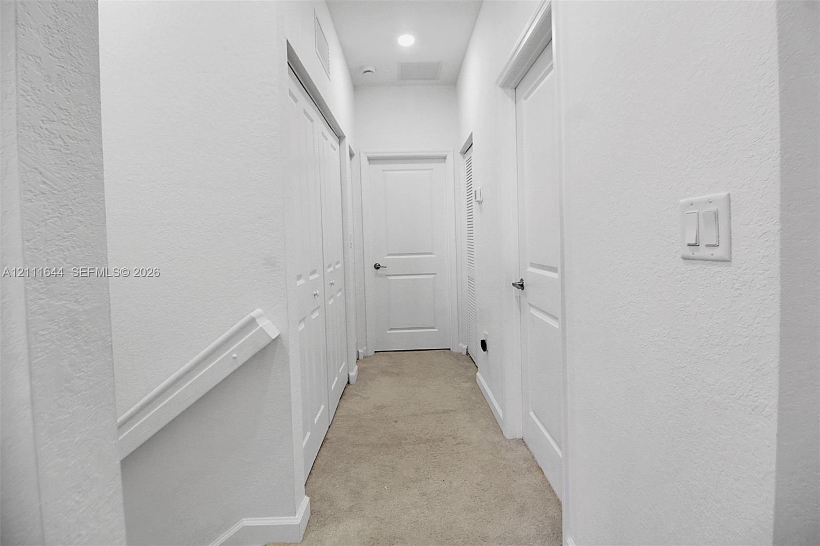 Hallway featuring neutral wall-to-wall carpeting, three paneled interior doors, a double-door closet, and recessed ceiling lighting