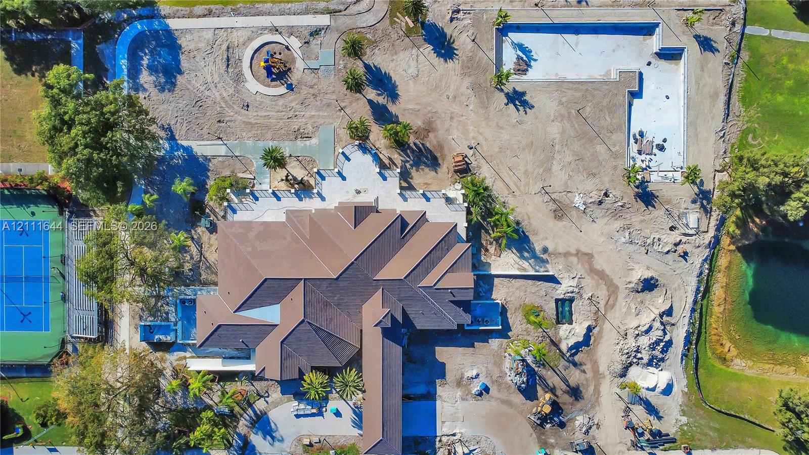 Aerial view of a sprawling property featuring a multi-gabled roofline, a dedicated tennis court, a large pool structure, and surrounding grounds