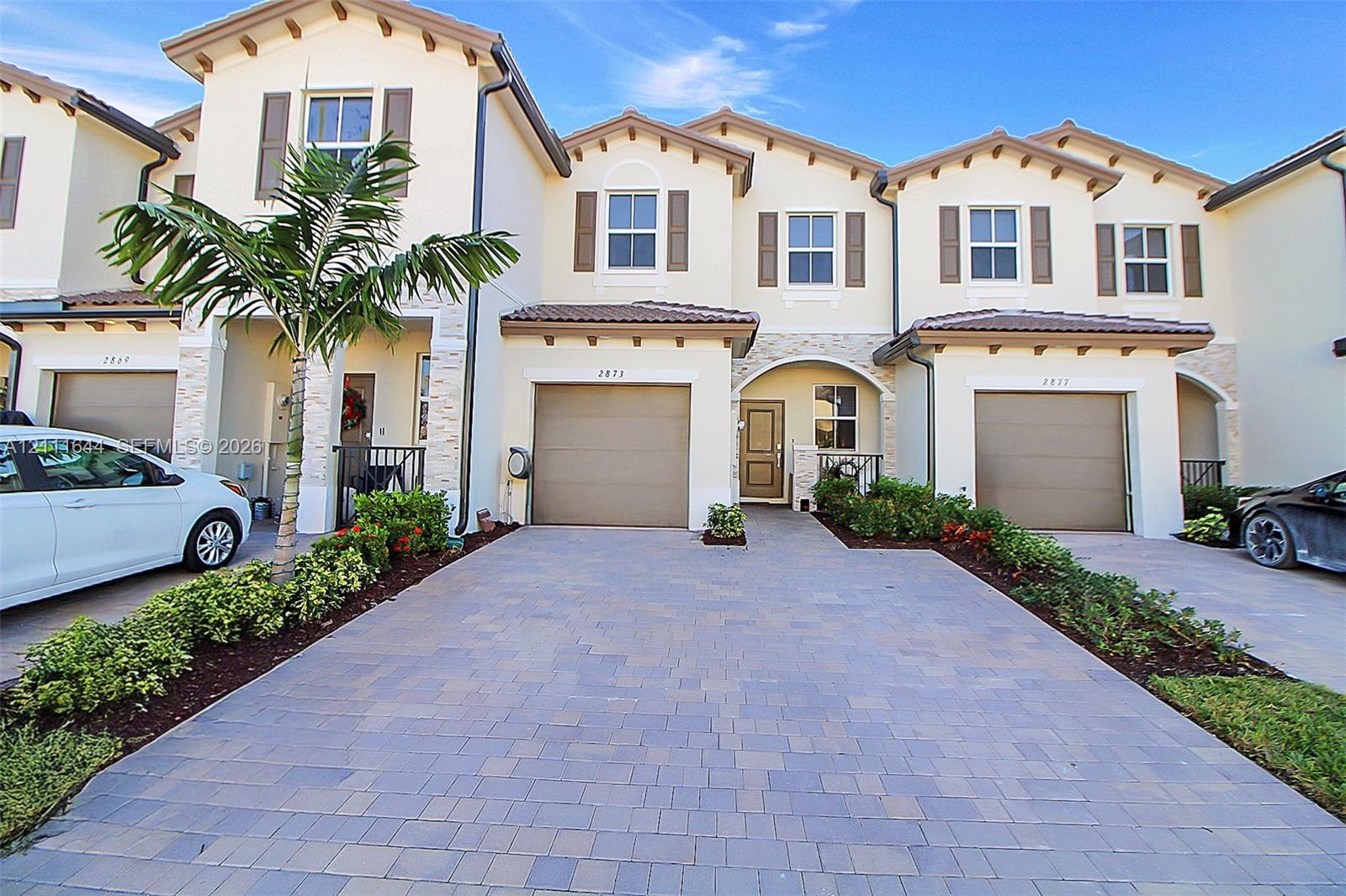 Mediterranean-style exterior featuring stucco siding, stone veneer accents, paver driveway, attached multi-car garages, and recessed entryways