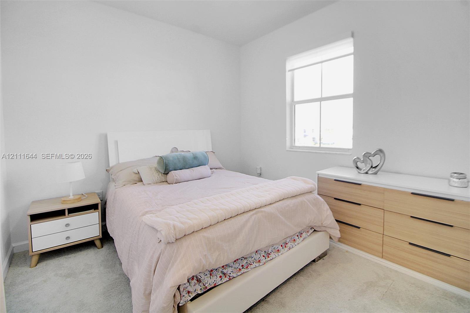 Neutral-toned interior space featuring light-colored wall-to-wall carpeting and a single-pane window with a roller shade