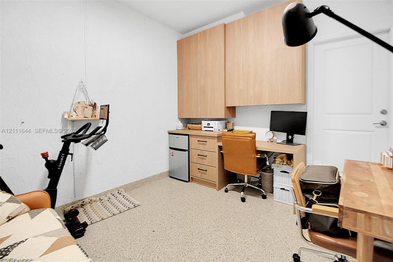 Built-in light-wood cabinetry with upper storage, integrated desk workspace with three drawers, and textured flooring