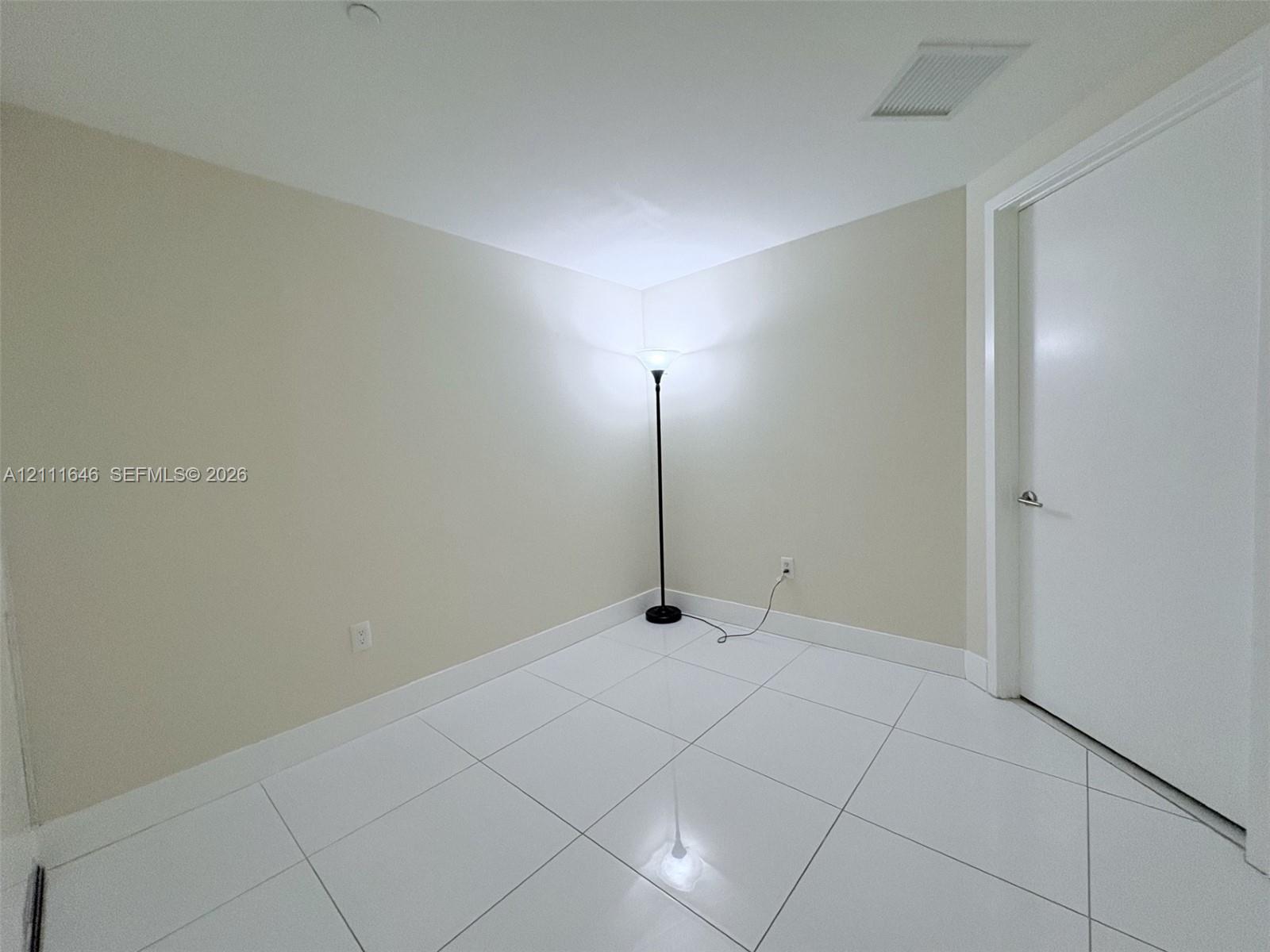 Neutral-toned walls, white large-format tile flooring, and a solid-core interior door with satin nickel hardware
