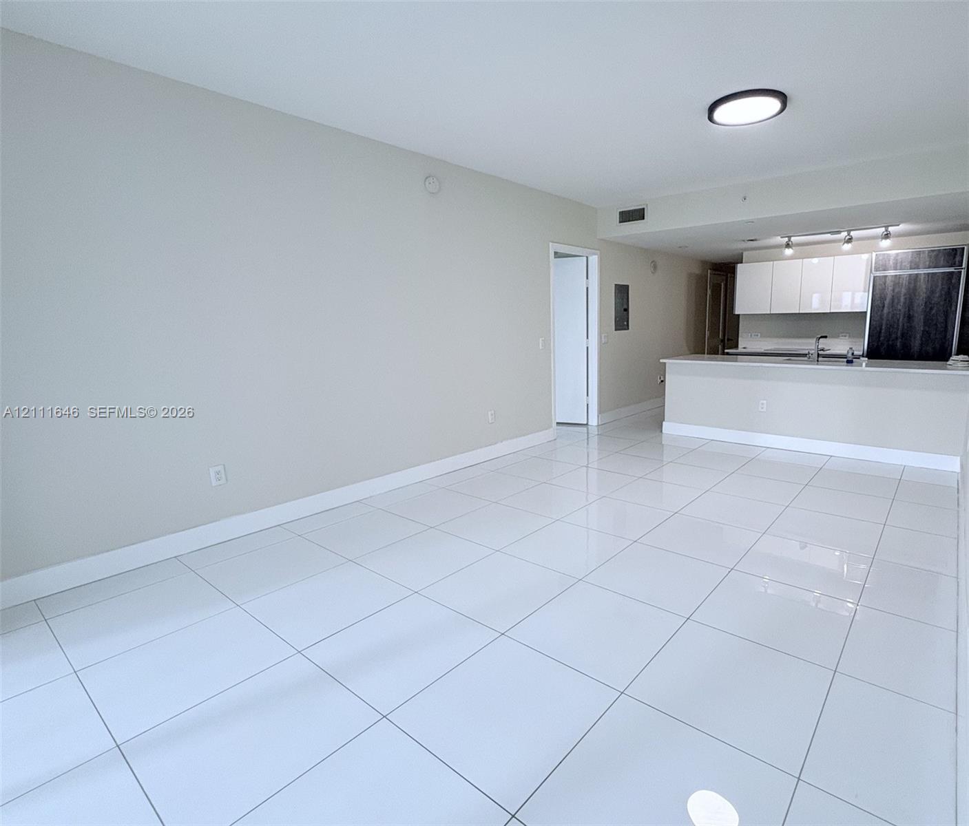 Large-format white tile flooring, high-gloss white cabinetry, integrated stainless steel kitchen appliances, peninsula countertop, and flush-mount lighting