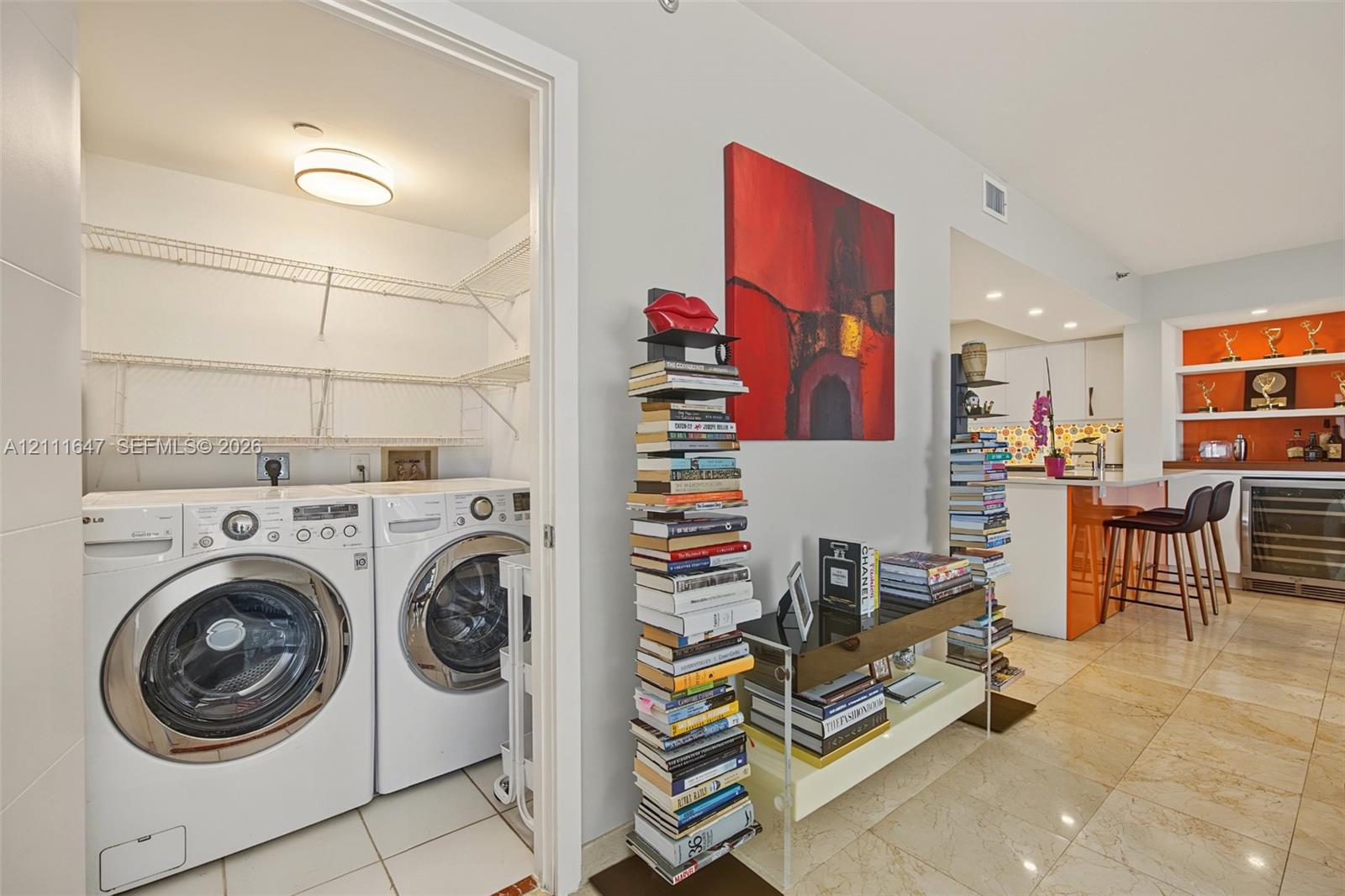 Dedicated laundry closet featuring built-in wire shelving and tile flooring, accompanied by kitchen cabinetry with a breakfast bar, under-cabinet lighting, and recessed shelving