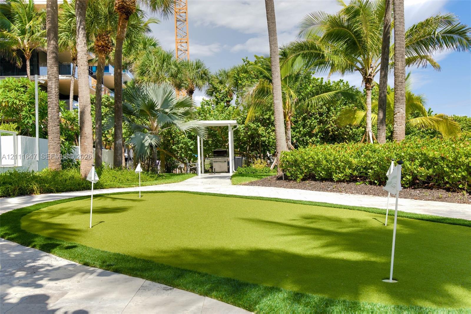 Putting green with synthetic turf surfacing, stone-paved walkways, and established palm trees
