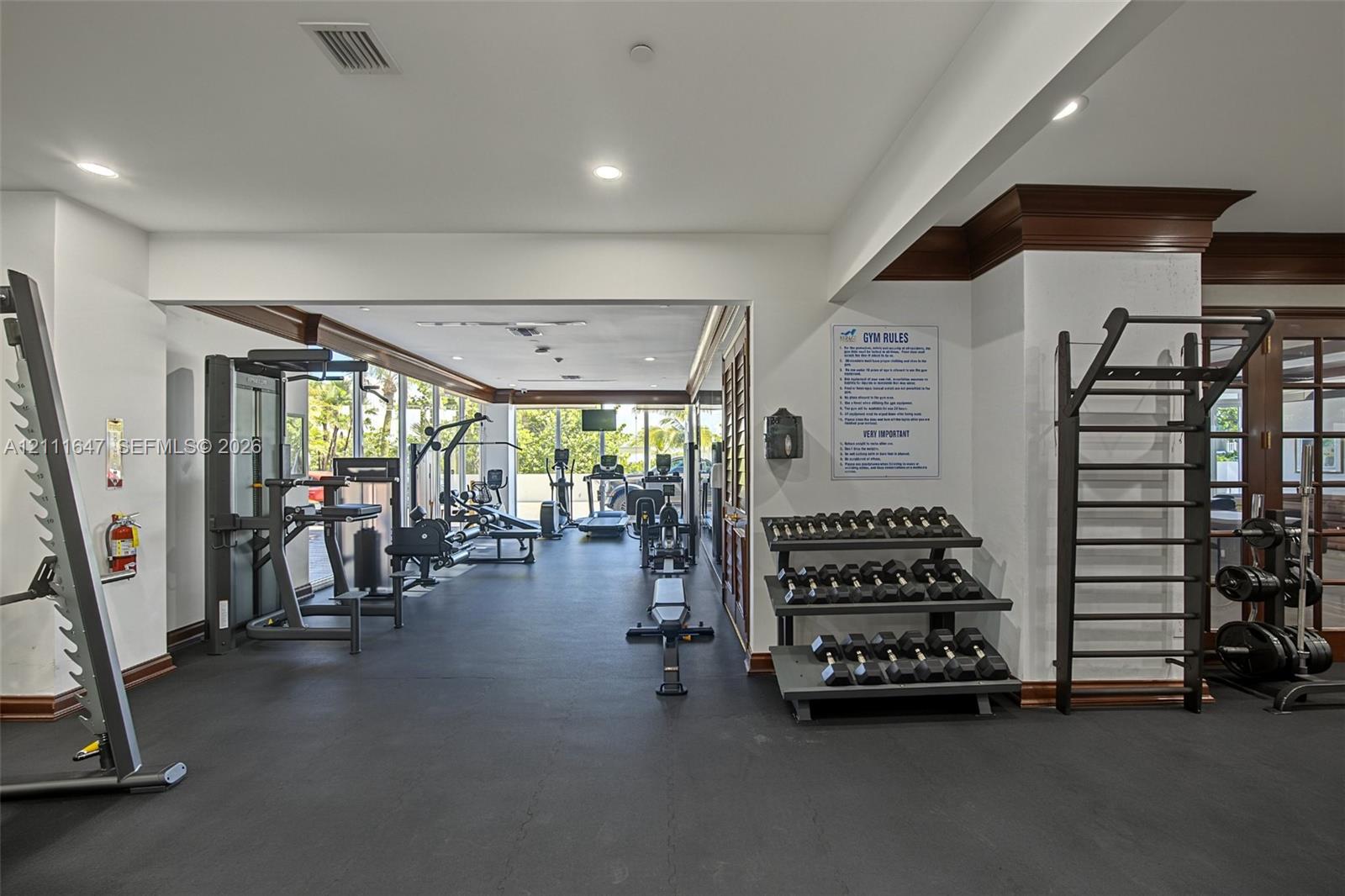 Fitness center featuring dark rubber flooring, recessed ceiling lighting, wall-mounted fitness equipment, and crown molding