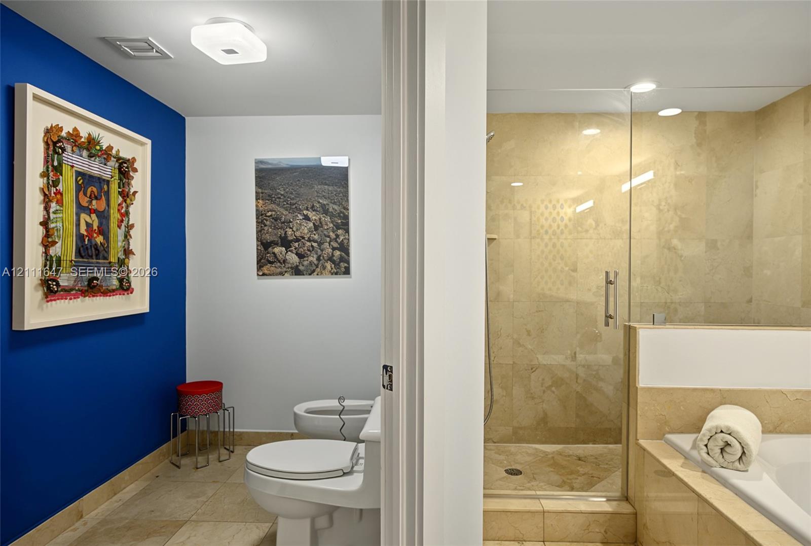 Full-height glass shower enclosure, stone-tiled flooring, stone wall cladding, built-in soaking tub, and flush-mount lighting