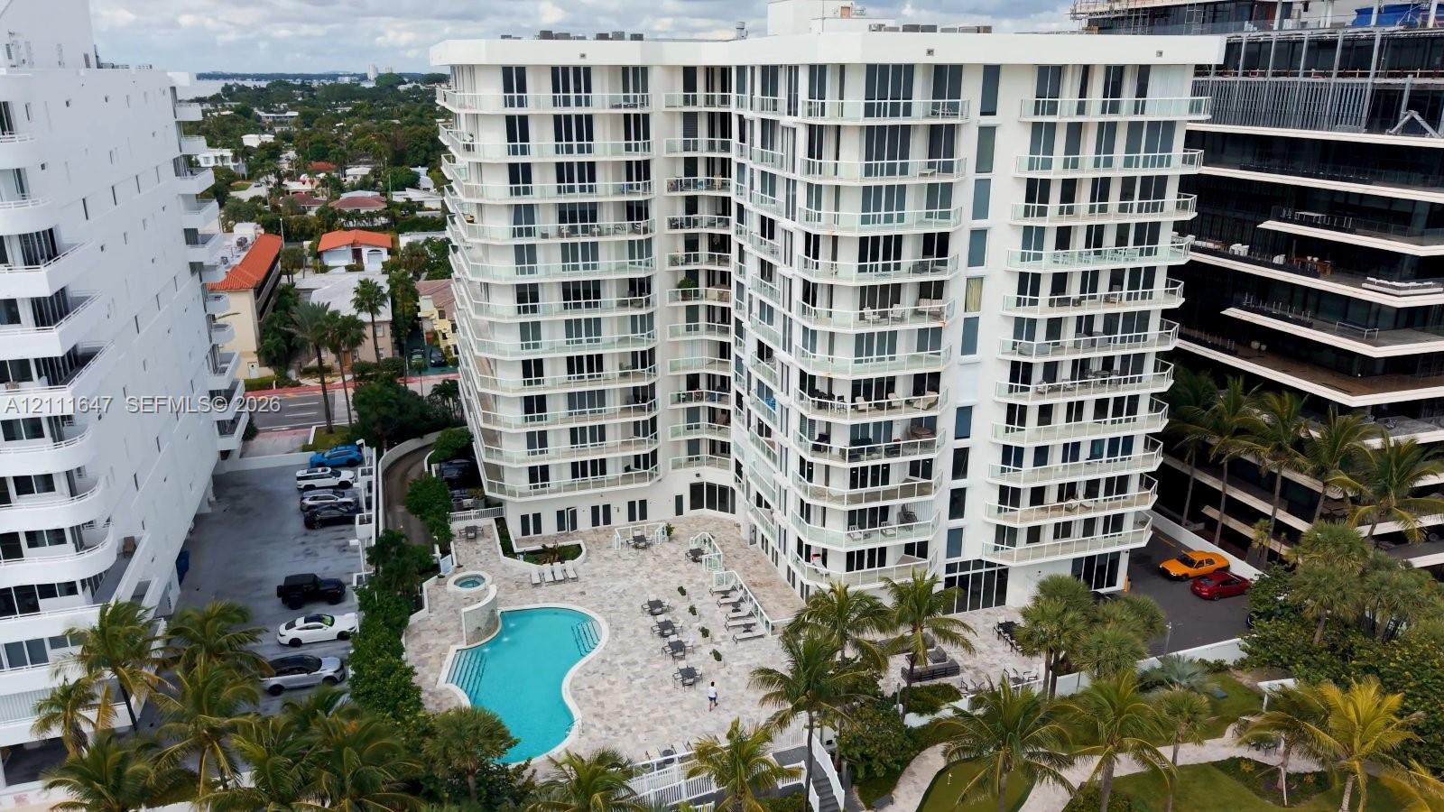 High-rise residential building featuring private balconies, an outdoor swimming pool, stone-paved patio, and mature palm trees