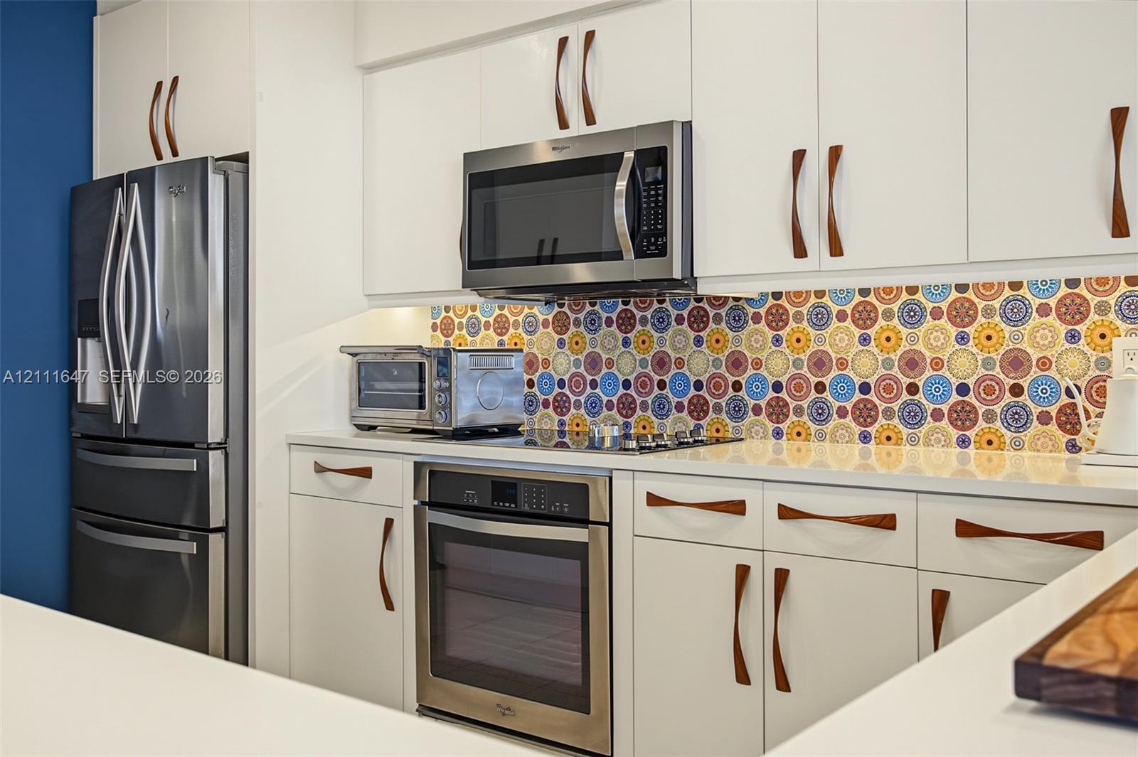 Kitchen featuring white cabinetry with wood-finish hardware, patterned tile backsplash, quartz countertops, and stainless steel appliances