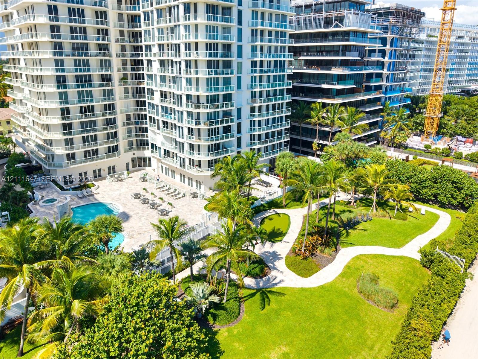 High-rise residential exterior featuring expansive paved pool deck, custom-shaped swimming pool, integrated spa, and manicured landscaping with mature palm trees
