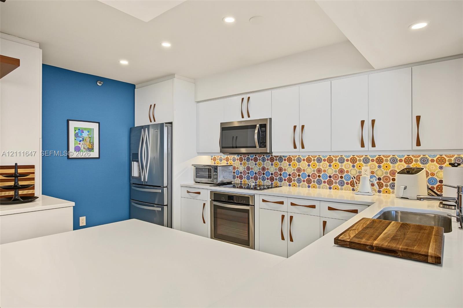 Kitchen featuring white cabinetry with integrated hardware, patterned tile backsplash, quartz countertops, stainless steel appliances, and recessed lighting