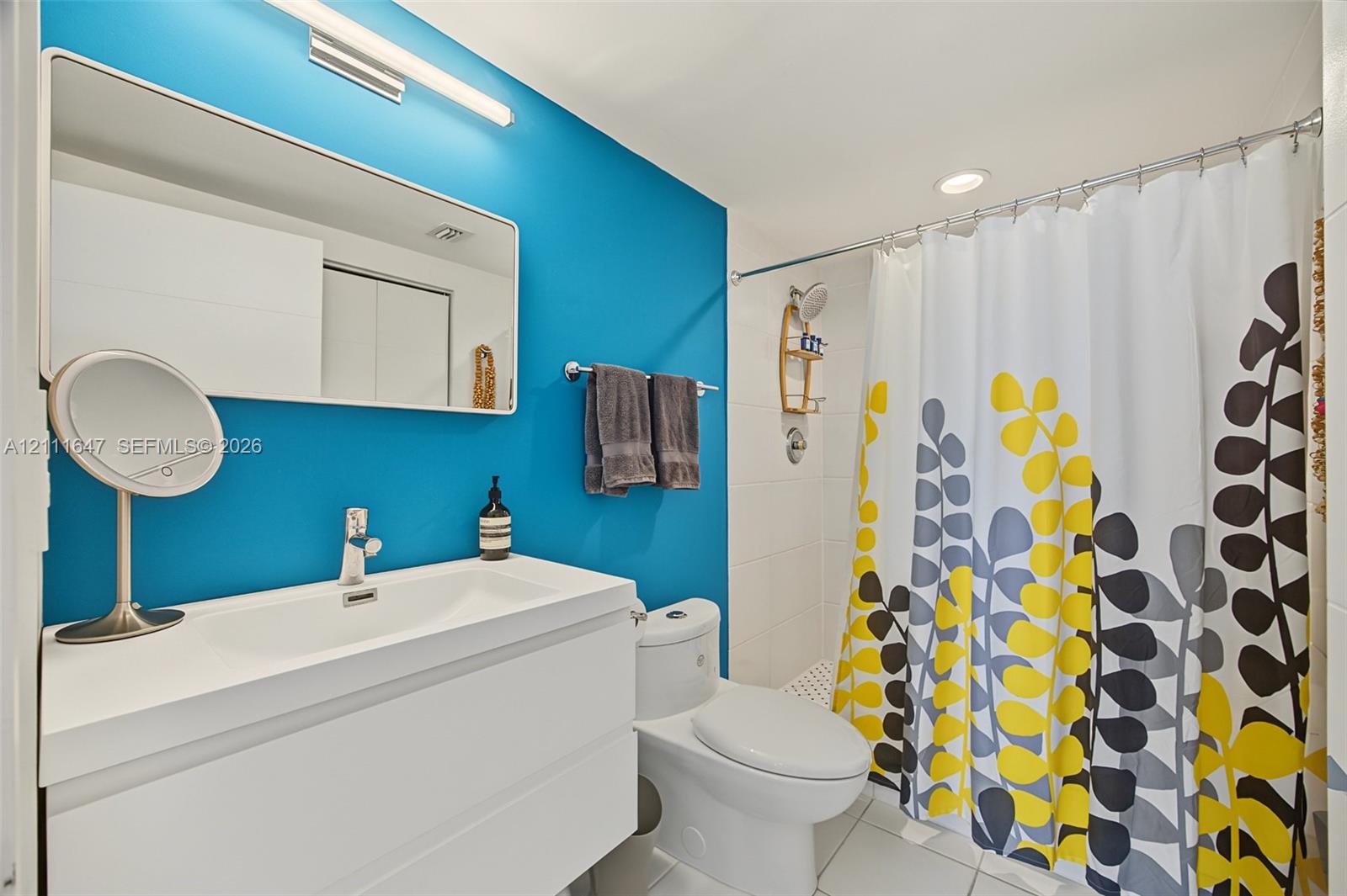 Wall-mounted rectangular mirror, white floating vanity with integrated sink, polished chrome single-handle faucet, and tiled shower surround