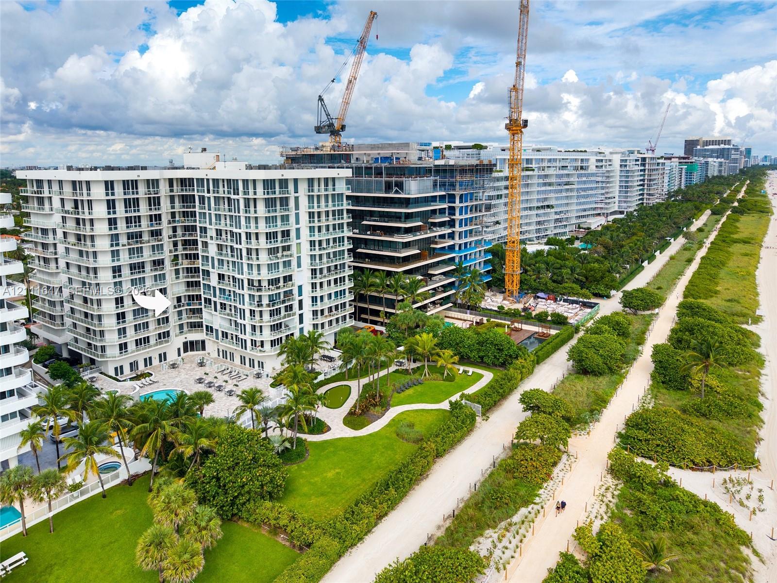 Multi-story residential complex featuring private pool, expansive manicured grounds, mature palm trees, and direct sand-beach access